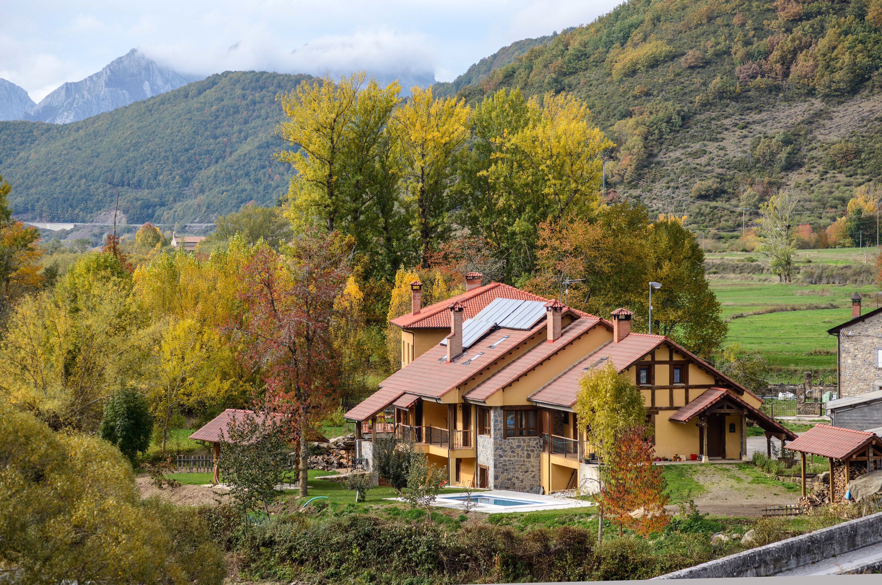 A traditional chalet with a sloped roof, a stone foundation, and a small swimming pool in the front yard.
