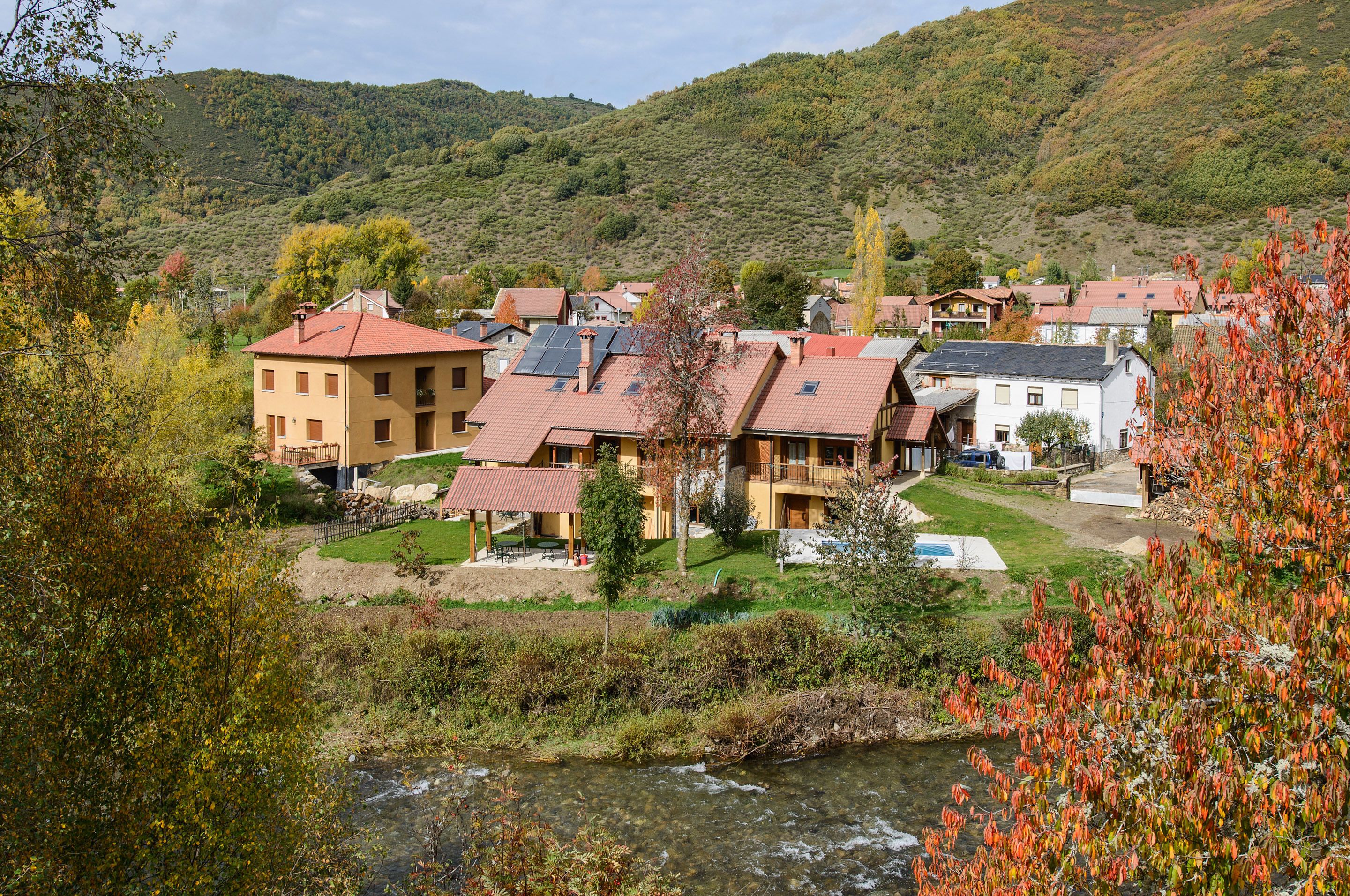 A hillside village with traditional buildings, a river, and a mountainous backdrop.