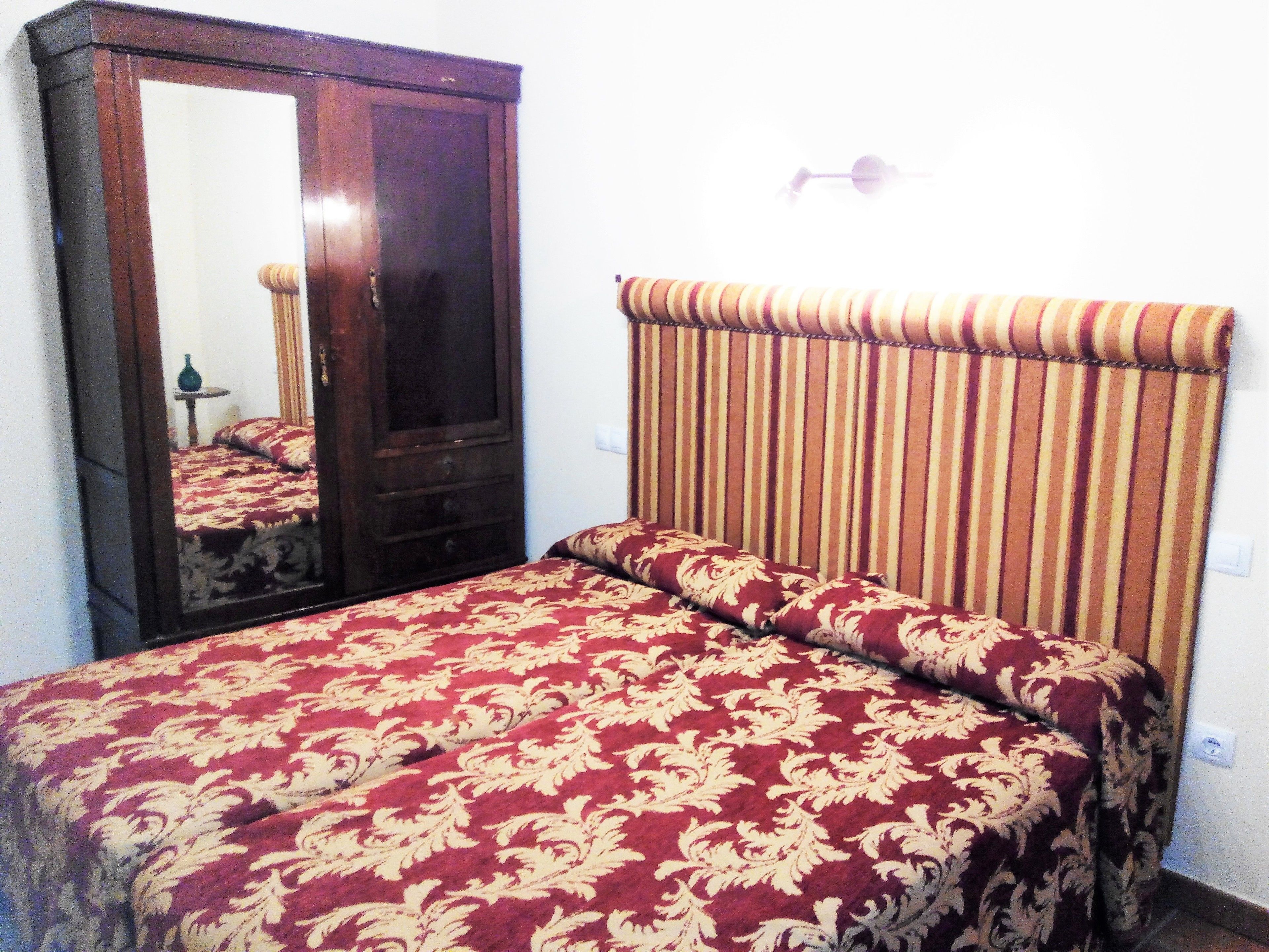 Um quarto com um espelho grande, uma cama com cabeceira listrada e uma mesa de cabeceira pequena.