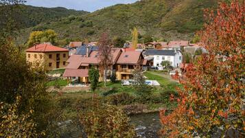 A hillside village with traditional architecture, a river in the foreground, and a mountainous backdrop.