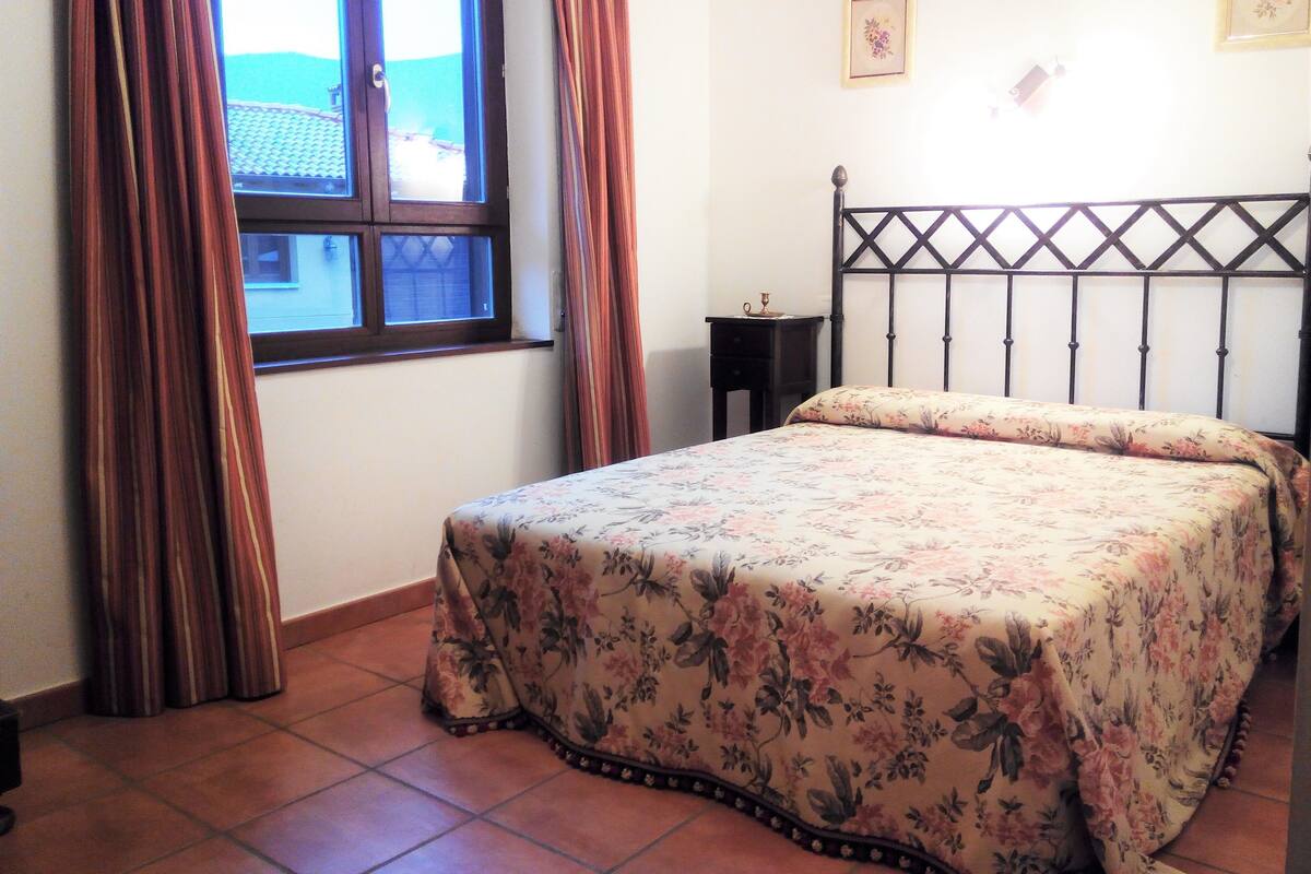 A bedroom with a bed, curtains, a nightstand, and a window.