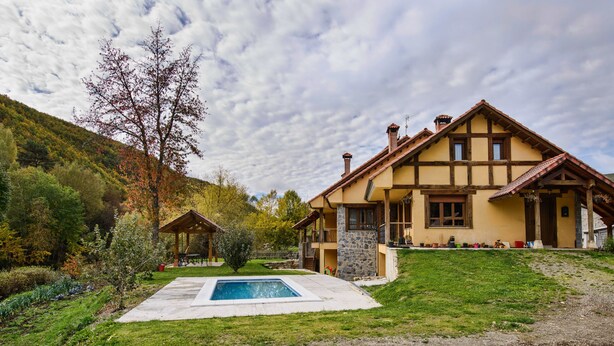A two-story house with a stone foundation, a wooden deck, and a swimming pool in the front yard. - El Casar del Puente (Boca de Huergano)