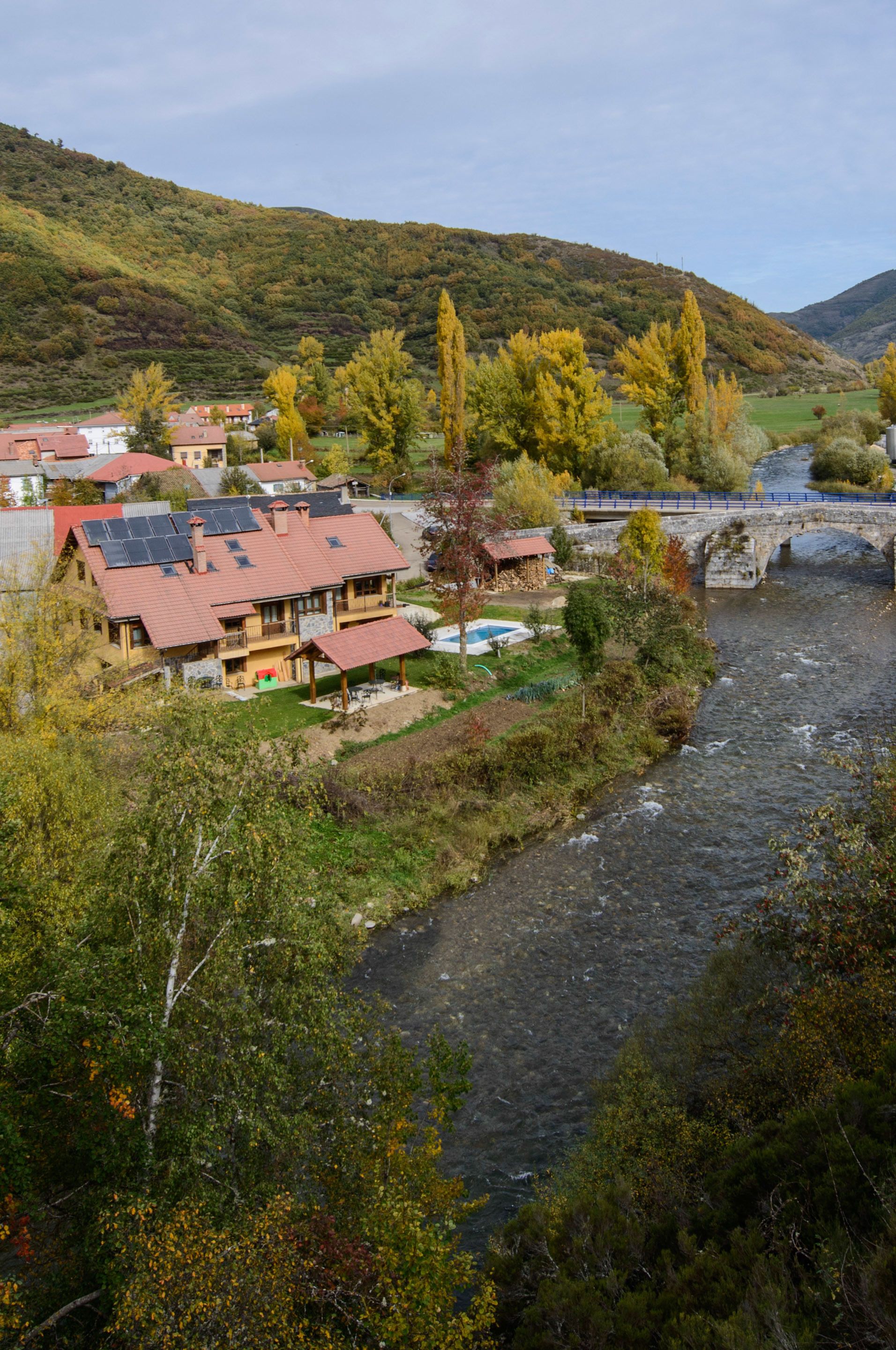 Un pueblo junto al río con casas, un puente y una colina al fondo.