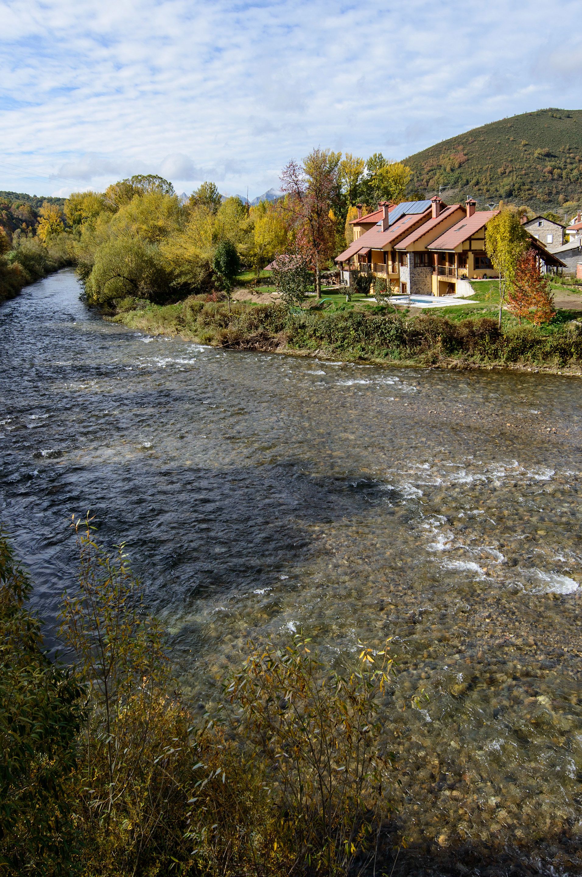 Un río serpenteando por un valle con casas en la ribera derecha.