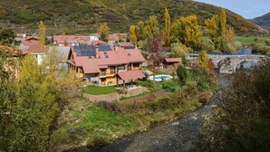 A hillside village with houses featuring red roofs and solar panels, a river, and a bridge. - El Casar del Puente (Boca de Huergano)