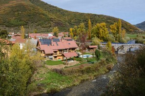 Uma vila numa encosta, com casas de telhados vermelhos e painéis solares, um rio e uma ponte.