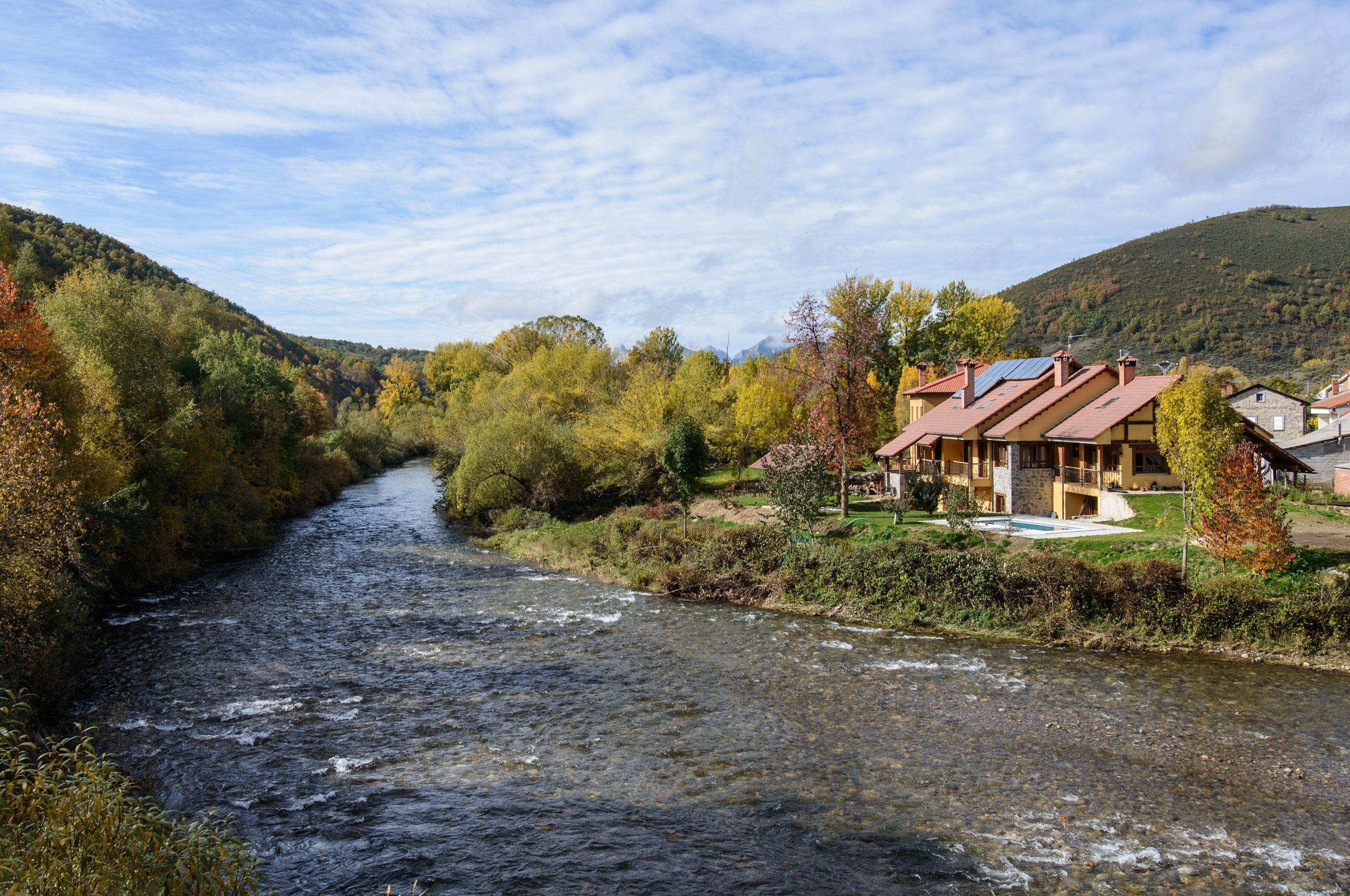 Un río fluye por un valle con casas a la derecha.