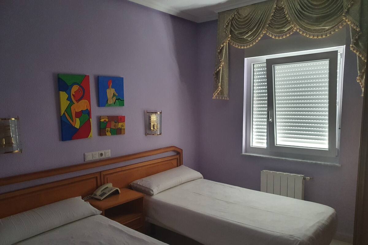 A room with two beds, a window with blinds, and wall art.
