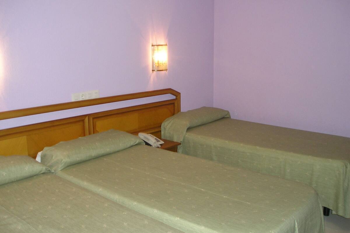 A room with two single beds, a wooden headboard, a bedside table with a phone, and a wall-mounted light fixture.