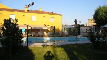 Un bâtiment jaune avec une piscine, une terrasse entourée d’une clôture et une enseigne sur laquelle on peut lire « INATTO ».
