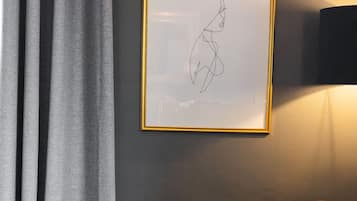 Una habitación con un cuadro abstracto enmarcado en la pared, una cortina gris y un sillón naranja.