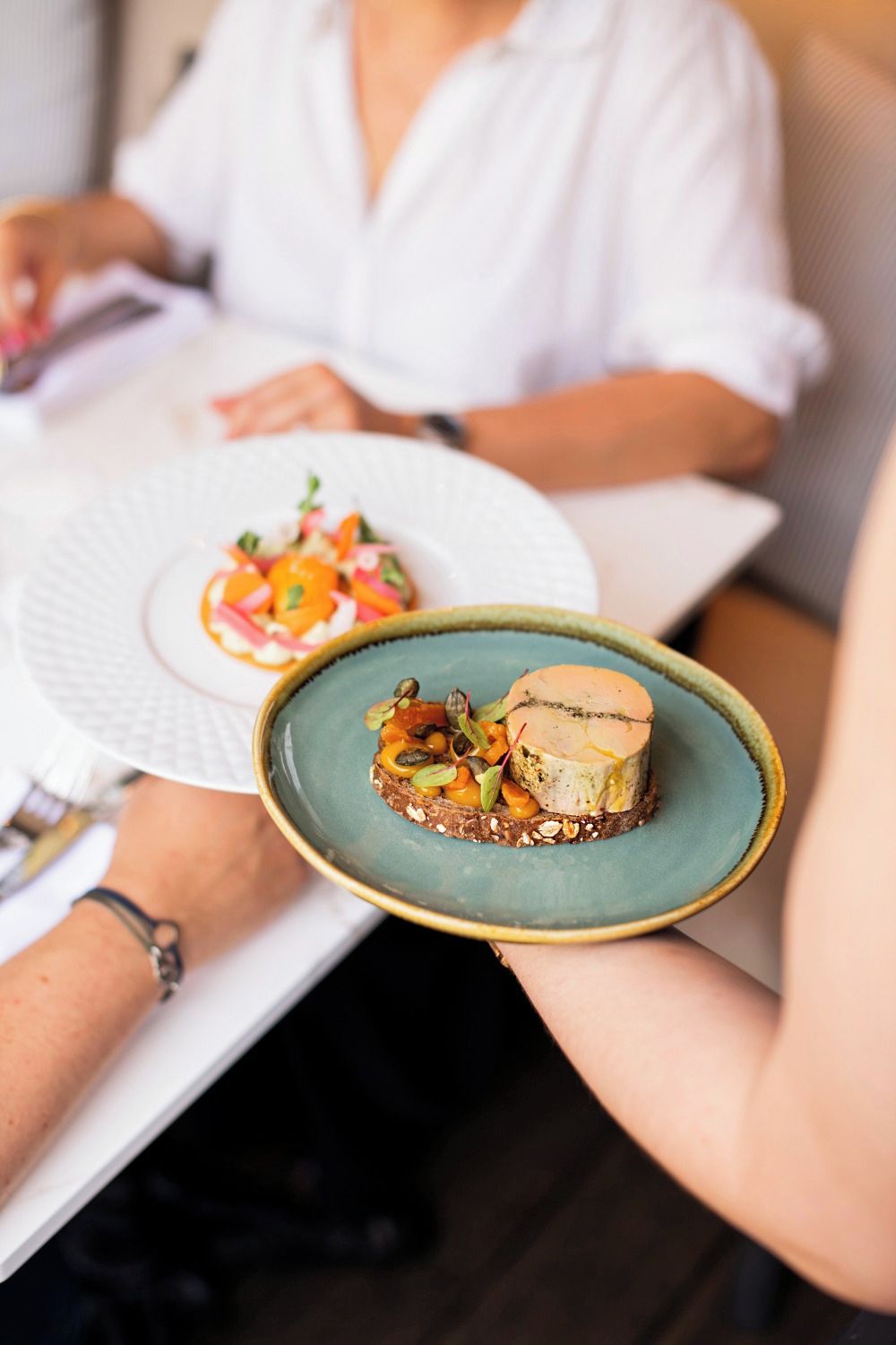 A person holding a plate with a dessert and a plate with a salad.