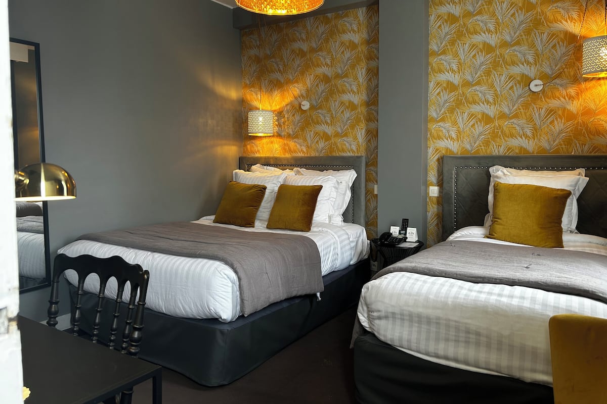 Une chambre d’hôtel avec deux lits, une petite table et un miroir.