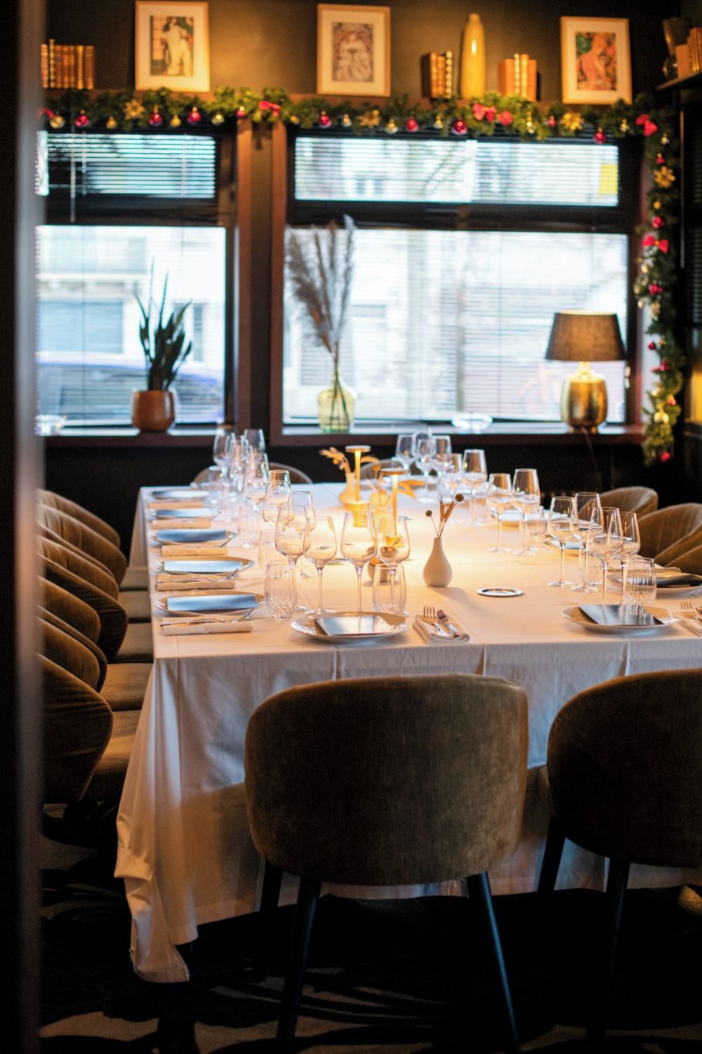 Una mesa de comedor dispuesta con platos, cubiertos y vasos, rodeada de sillas tapizadas.