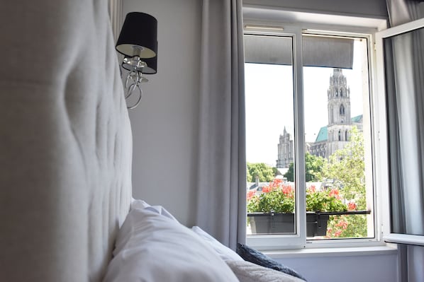 A hotel room with a bed, a window with a view of a church and flowers outside.