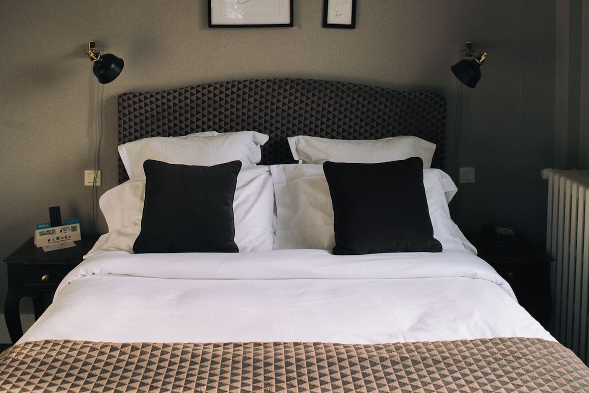 Un lit bien fait, recouvert d’une couvre-lit à motifs, avec une tête de lit au design géométrique et deux œuvres d’art encadrées accrochées au mur.