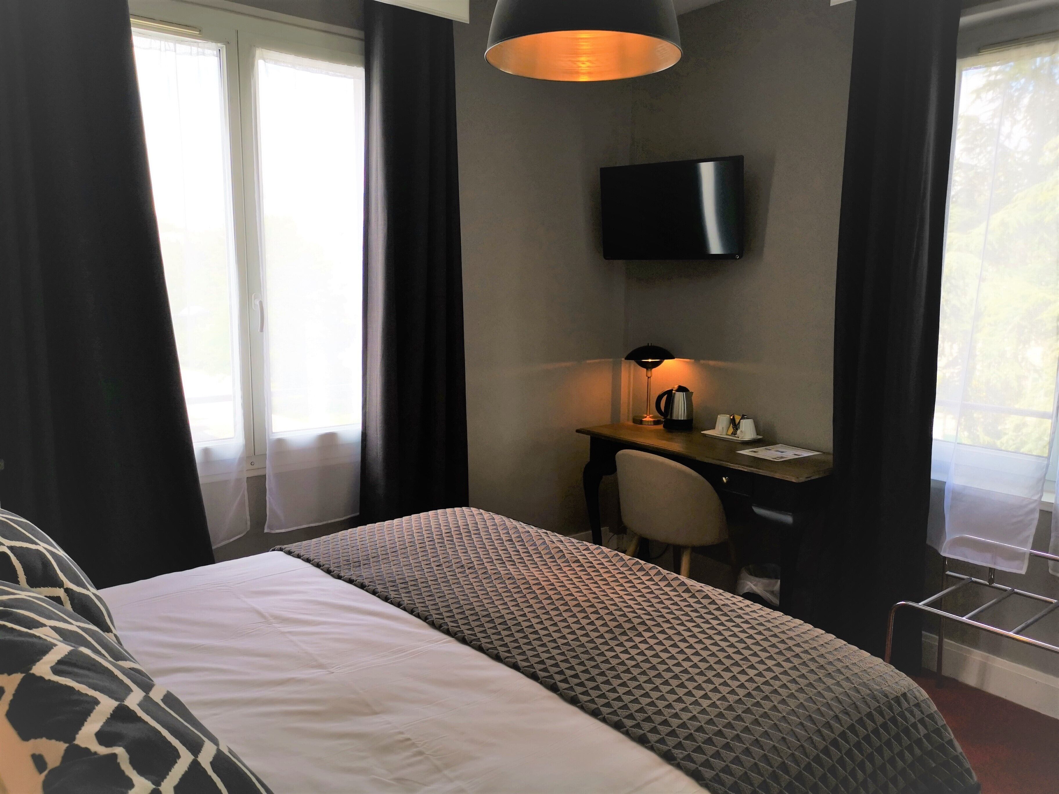 Hotellihuone, jossa on sänky, työpöytä, tuoli, seinälle asennettu televisio ja ikkuna, jossa on verhot.