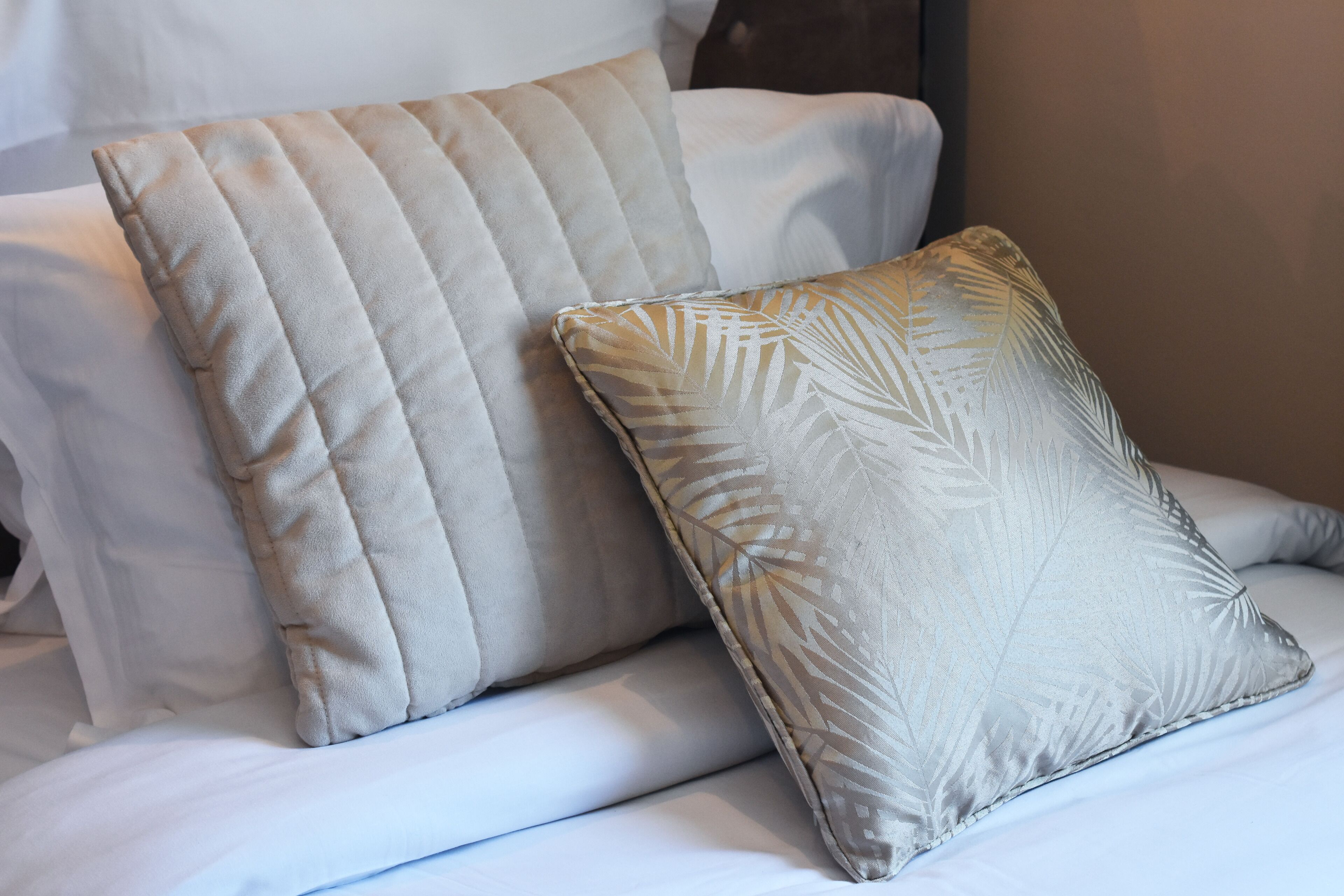 A bed with two pillows, one with a leaf pattern and the other with a quilted design.