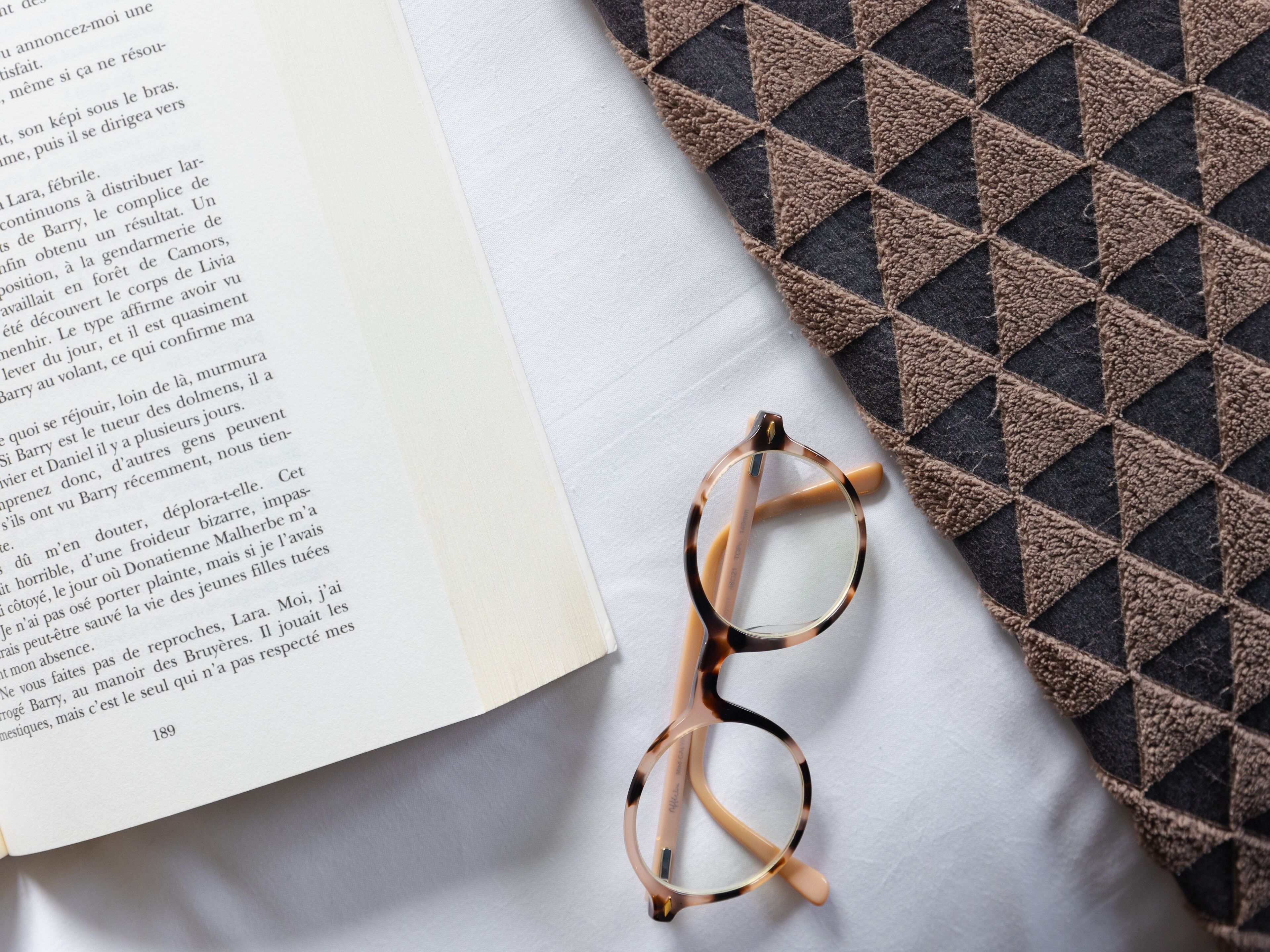A book open on a white surface with a pair of glasses beside it.