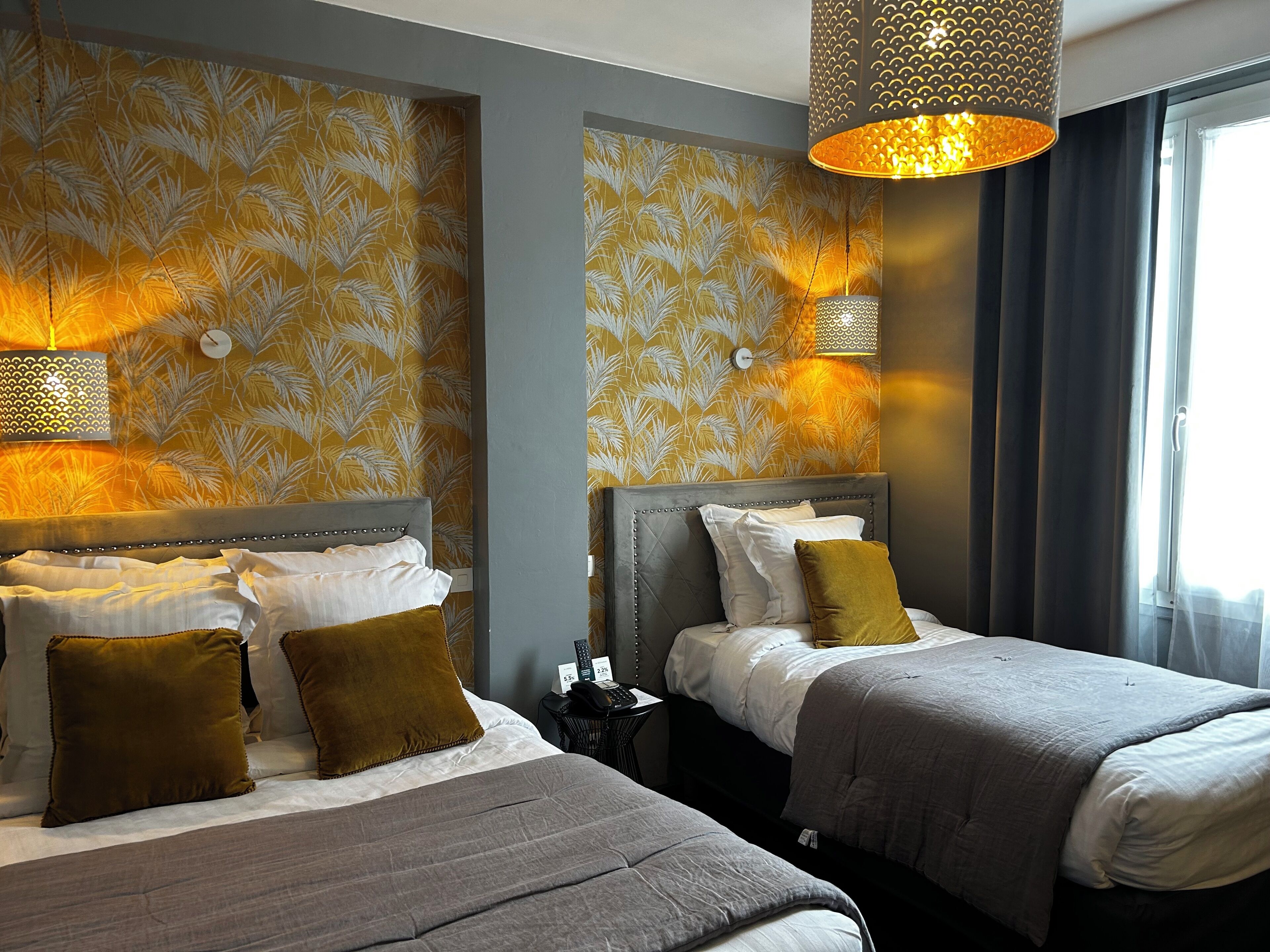 A hotel room with two beds, patterned wallpaper, and a large window with curtains.