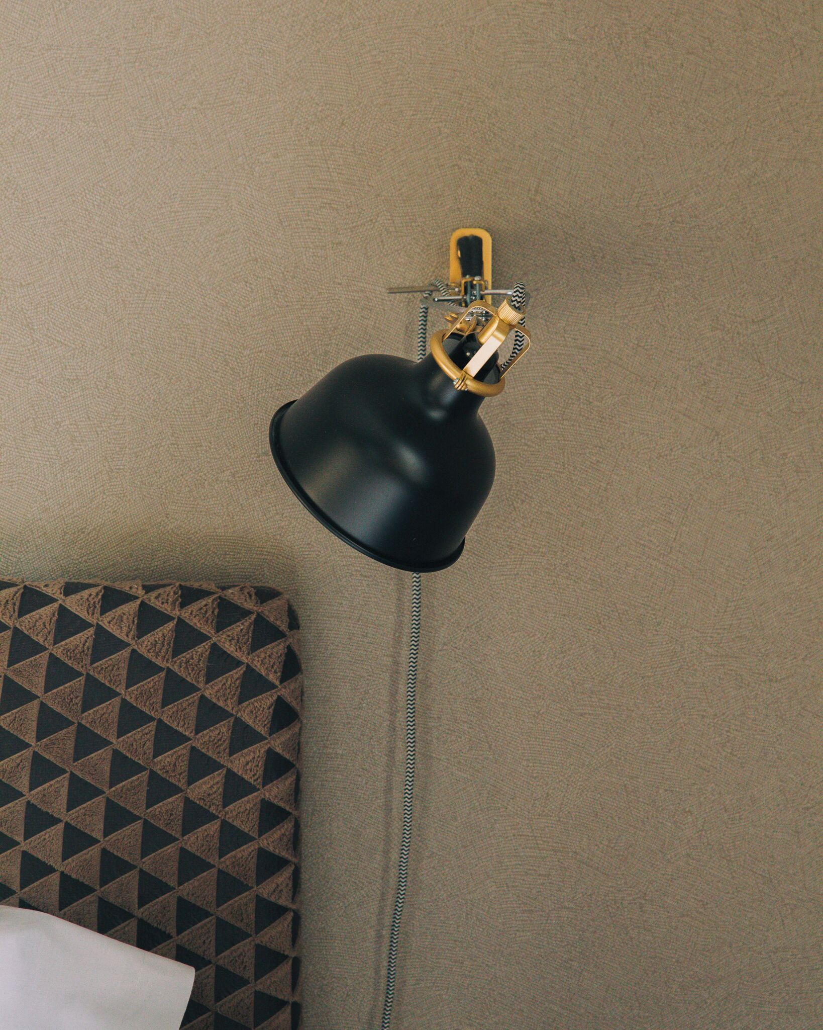 Una lámpara de escritorio negra con cuello flexible sobre una pared beige con textura.