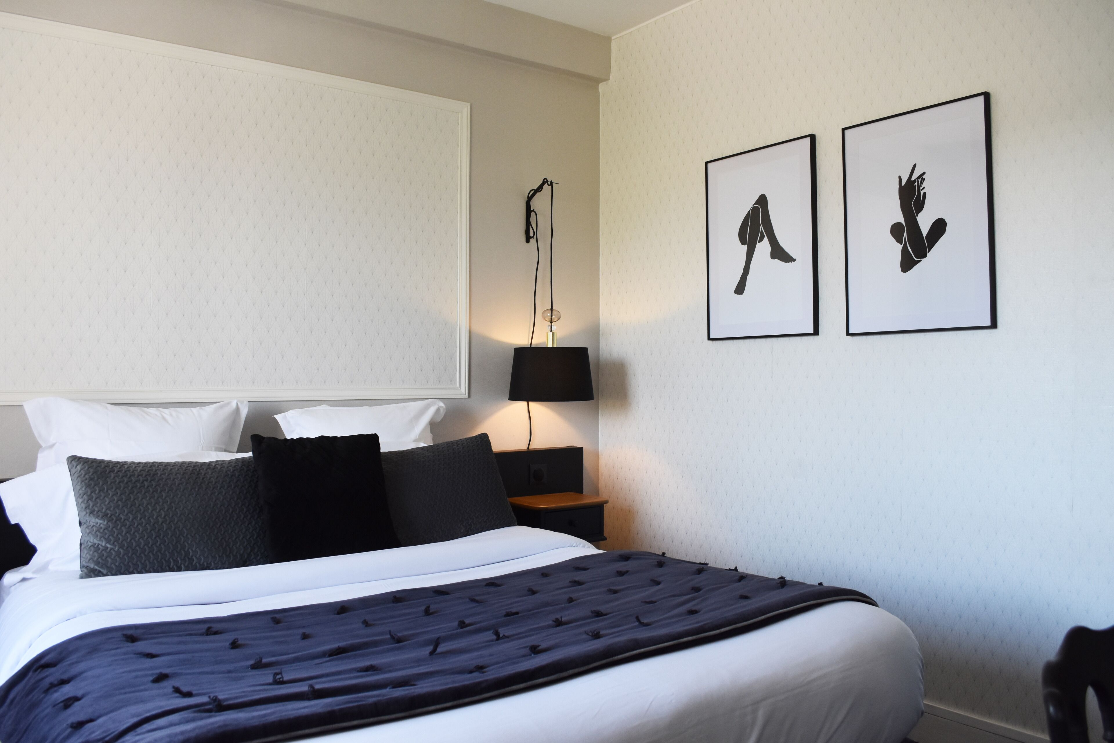 A neatly made bed with a dark blue bedspread and multiple pillows, a bedside lamp, and two framed artworks on the wall.