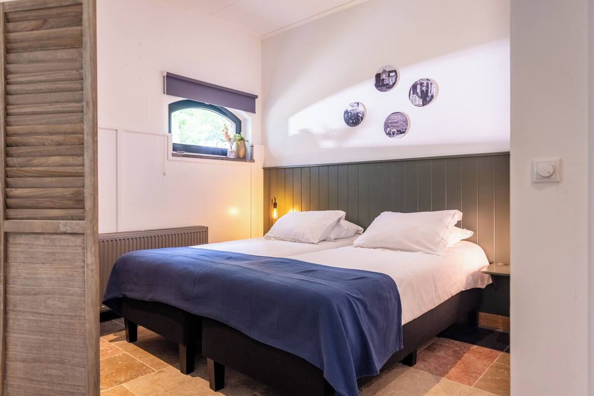 A bedroom with a bed, a window with a view, a wall-mounted shelf with decorative items, and a wall with circular mirrors.