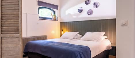 Un dormitorio con cama, ventana con vistas, estante de pared con objetos decorativos y pared con espejos circulares.