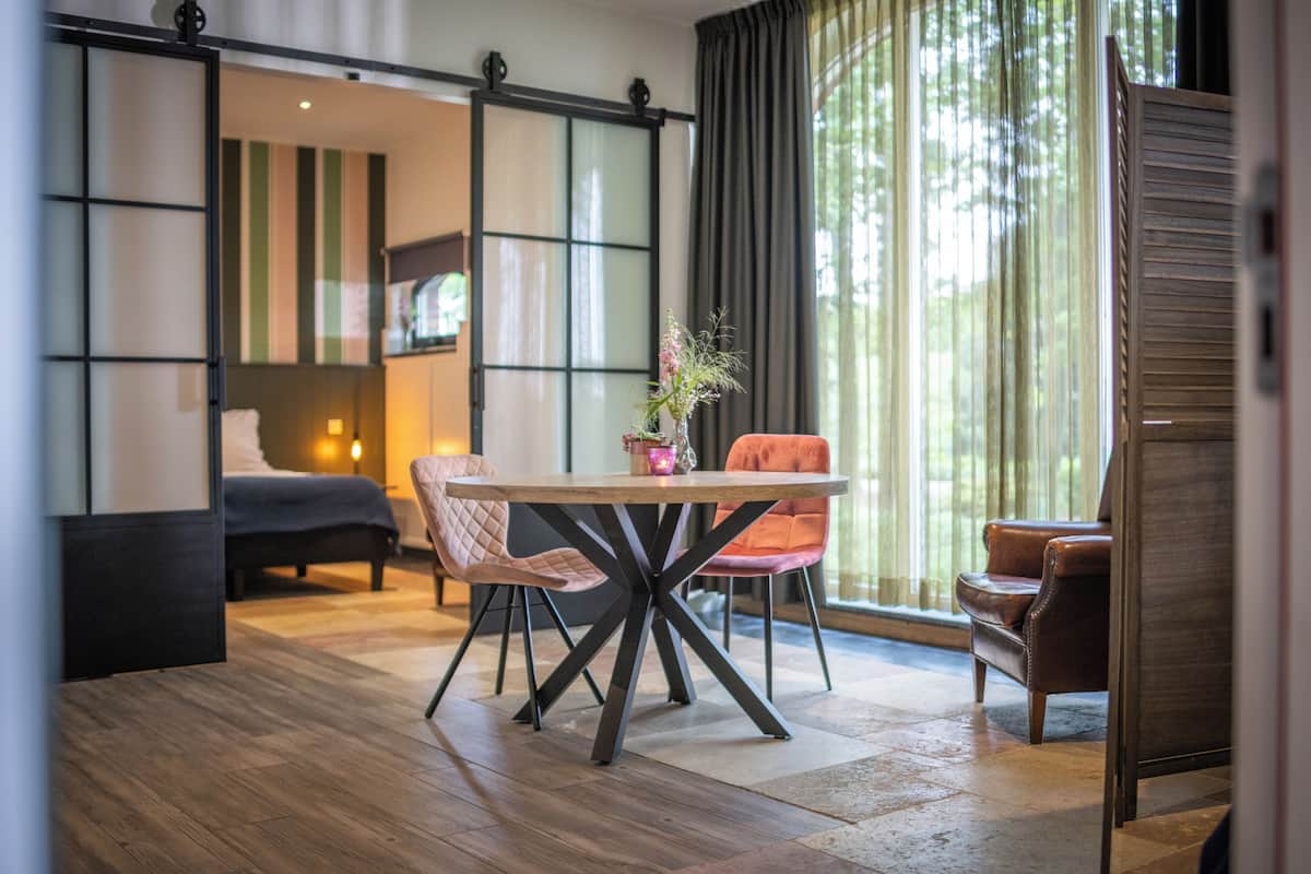 A modern hotel room with a wooden floor, a round table with chairs, a bed, and a sliding shoji screen.