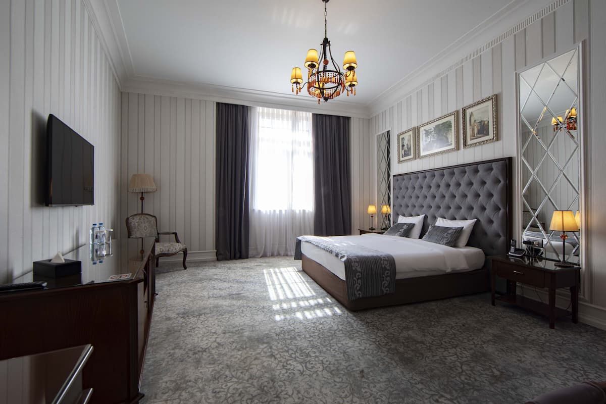 A hotel room with a large bed, a desk, a chair, a chandelier, and a large mirror.