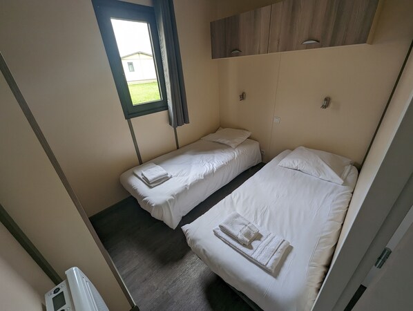 A room with two single beds, a window with curtains, a wooden headboard, and a small heater. - Lodge-Hôtel & Spa les Voiles du Grand Large (Meyzieu)