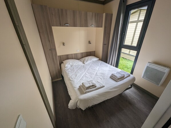 A modern bedroom with a wooden headboard, a large bed, and a window with curtains. - Lodge-Hôtel & Spa les Voiles du Grand Large (Meyzieu)