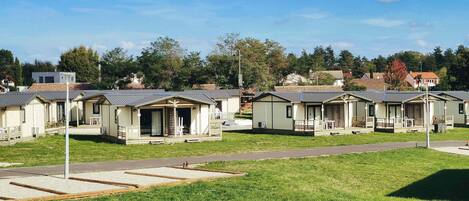 A row of mobile homes with individual porches and attached garages, set in a grassy area with a paved path in front.