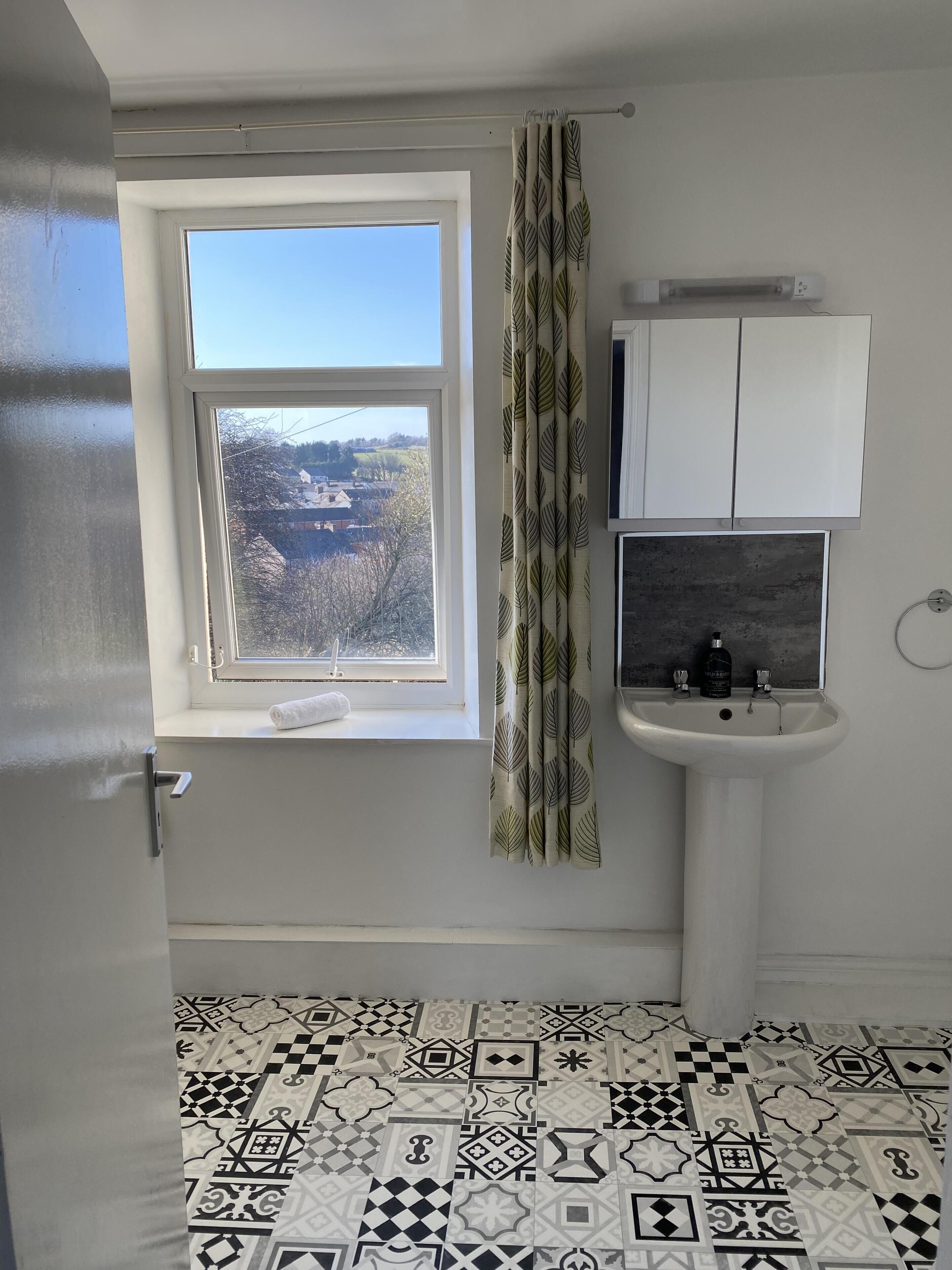 A bathroom with a window, a sink, and patterned floor tiles.