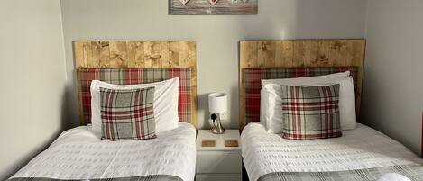 A double room with two beds, each with plaid bedding and matching pillows. There is a wooden headboard on each bed, and a wall-mounted decoration above the beds.