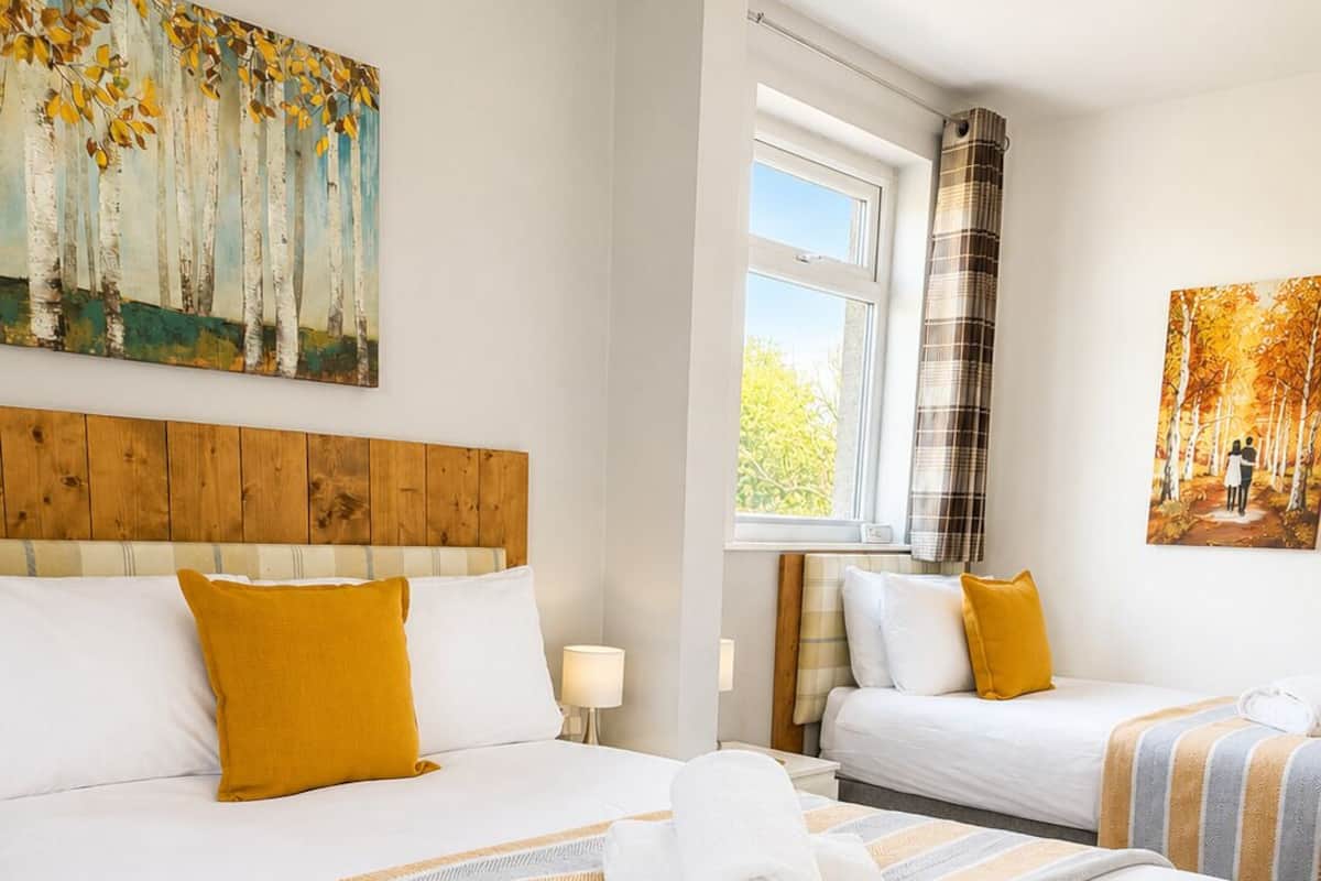 A hotel room with two beds, a wooden headboard, a window with curtains, and paintings on the walls.