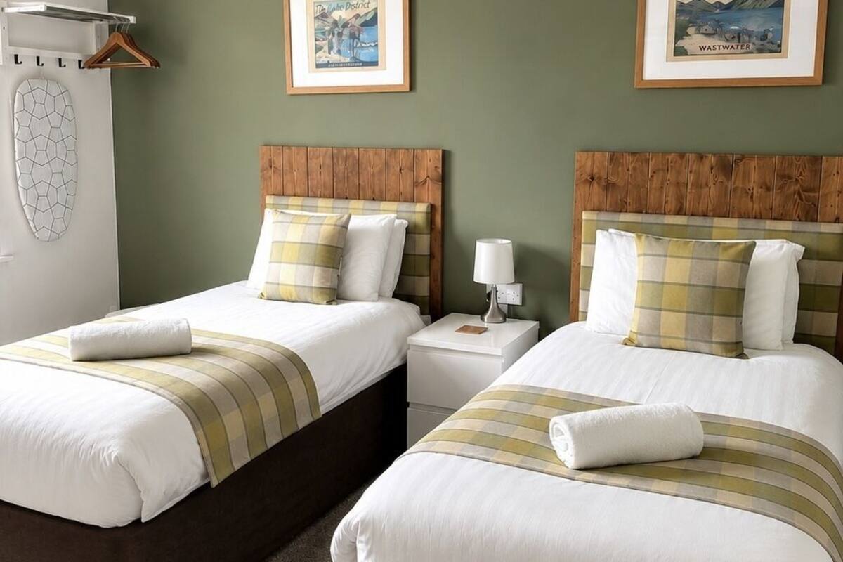A hotel room with two beds, a hanging light fixture, and two framed pictures on the wall.