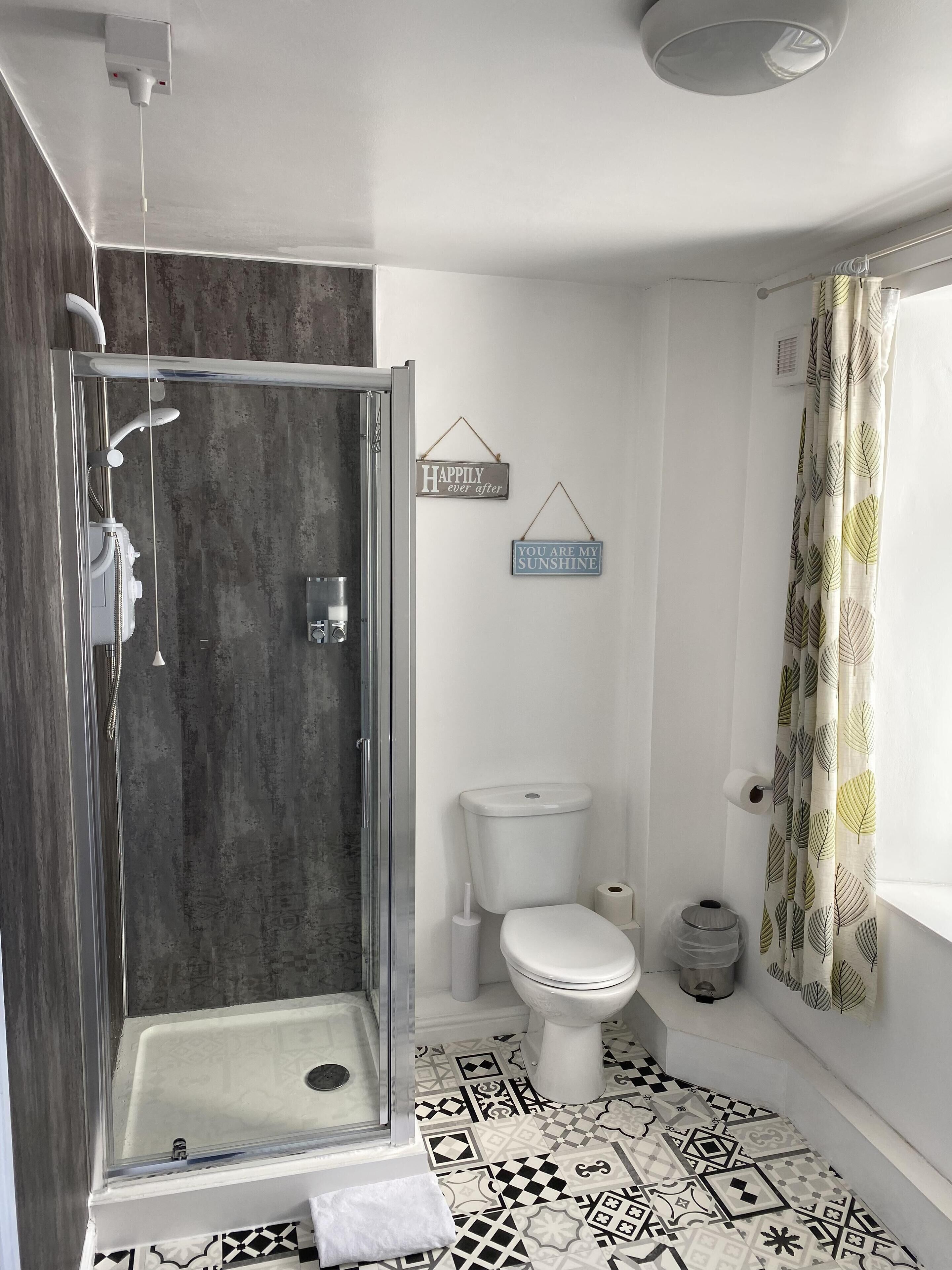 Une salle de bain moderne avec une douche à parois de verre, des toilettes et un lavabo. Des panneaux décoratifs ornent le mur, et des rideaux à motifs complètent l’ensemble.