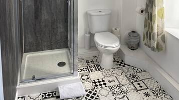 A modern bathroom with a glass-enclosed shower, a toilet, and a sink. There are decorative signs on the wall and patterned curtains.