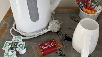 A white kettle, a mug, a container with coffee pods, and a small biscuit packet on a tray.