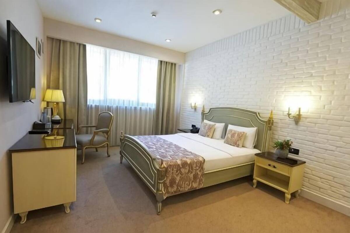 A hotel room with a bed, bedside table, lamp, chair, and a TV on a dresser.
