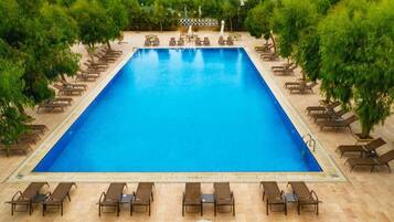 Una piscina rectangular con sillones de playa y sombrillas alrededor.