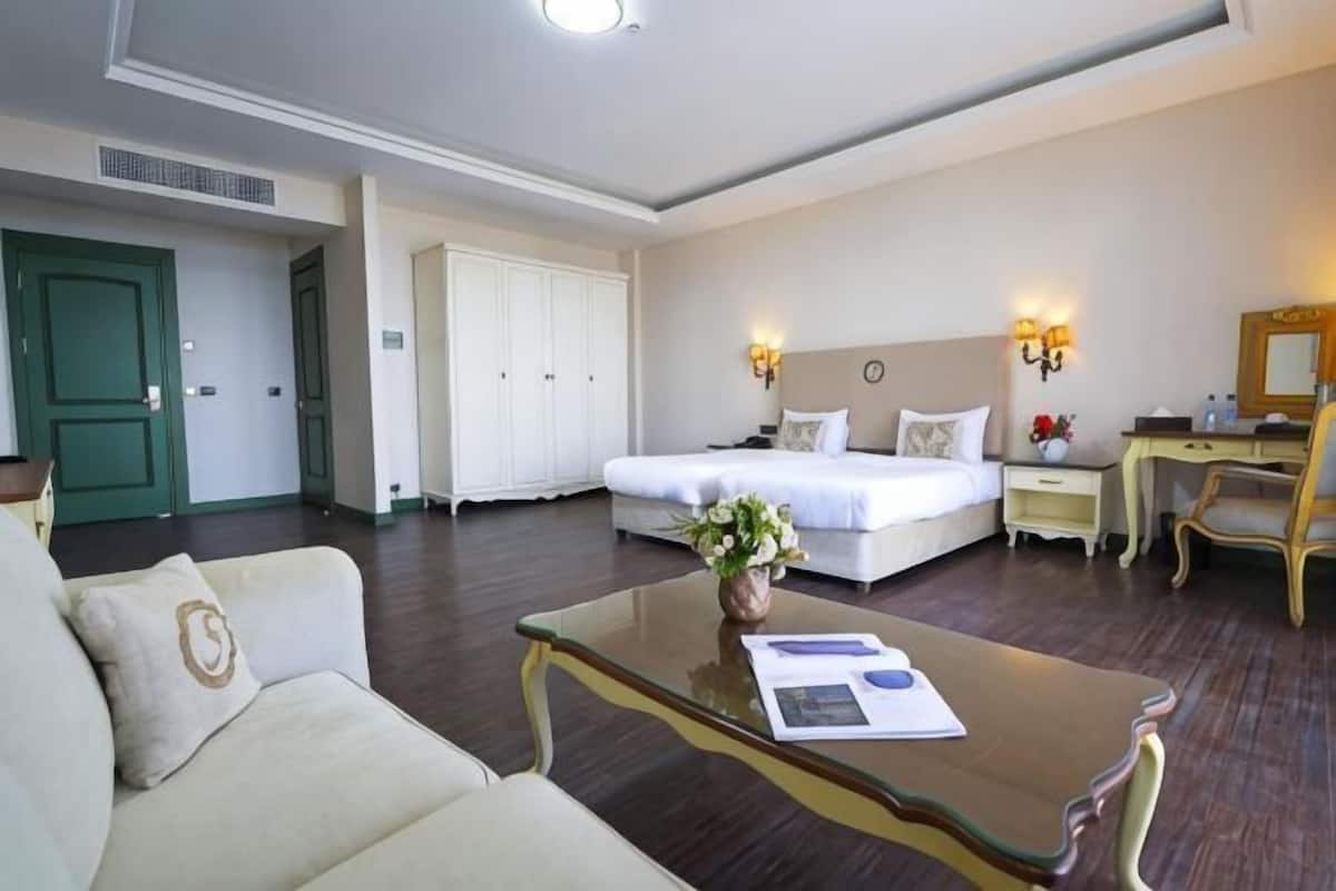 A hotel room with a bed, a sitting area with a sofa, a desk, and a chair.