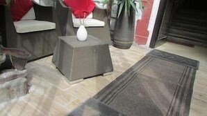 A room with a tiled floor, a small white vase on a textured stool, a potted plant, and a dark rug. - Hotel Ambra (Milano)