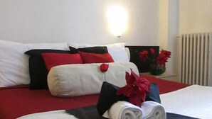 A hotel room with a neatly made bed, red and white bedding, and a vase with red flowers on the nightstand. - Hotel Ambra (Milano)