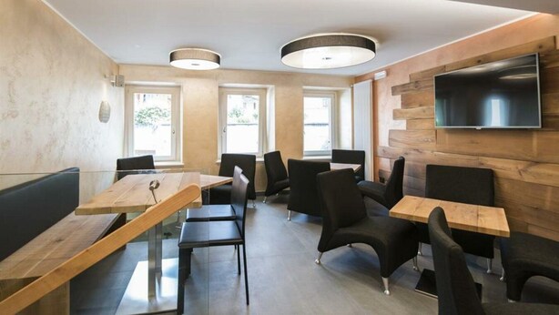 A modern dining area with wooden tables and black chairs, large windows, and a flat-screen TV mounted on the wall. - Hotel Ambra (Milano)