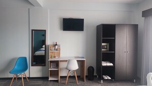 Een hotelkamer met een bureau, twee stoelen, een televisie, een kledingkast en een spiegel.