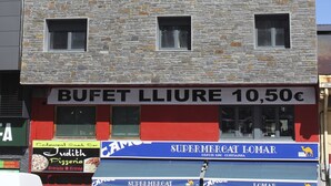 Un edificio de varios pisos con fachada de piedra, múltiples ventanas y letreros que indican un bufé y un supermercado.
