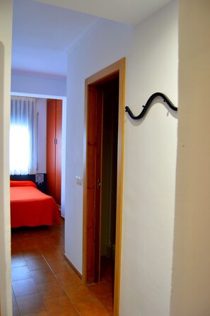 Ein Flur, der zu einem Schlafzimmer führt, mit roter Bettdecke, Holztür und einem schwarzen Wandhaken.