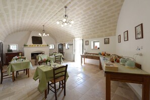 A spacious dining area with high ceilings and a fireplace, featuring multiple dining tables and chairs. - Masseria Lamiola Piccola (Ostuni)
